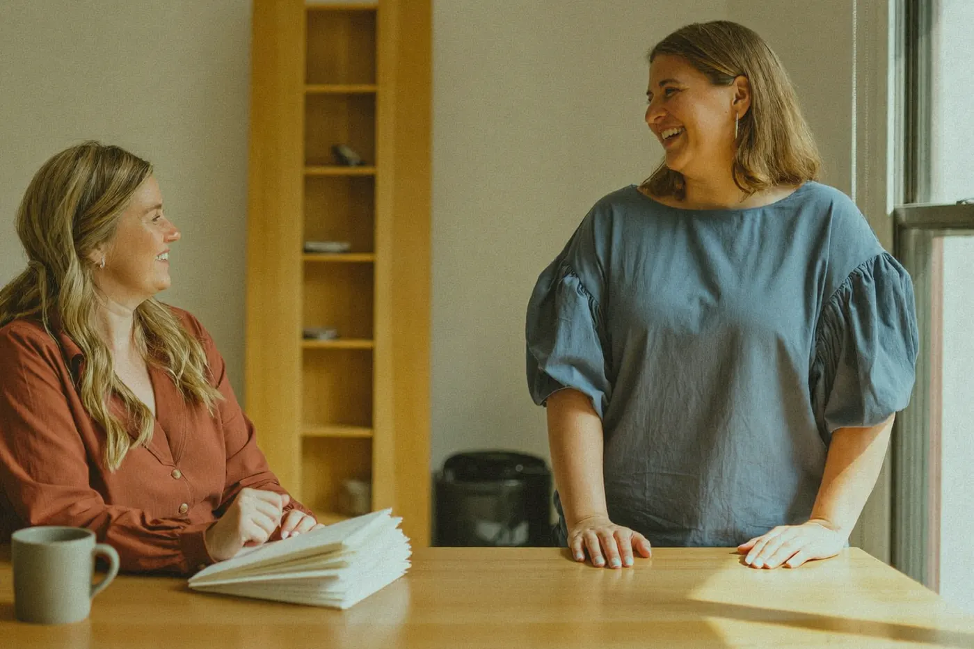 Practice manager and colleague in easy conversation over paperwork at a clinic front desk.