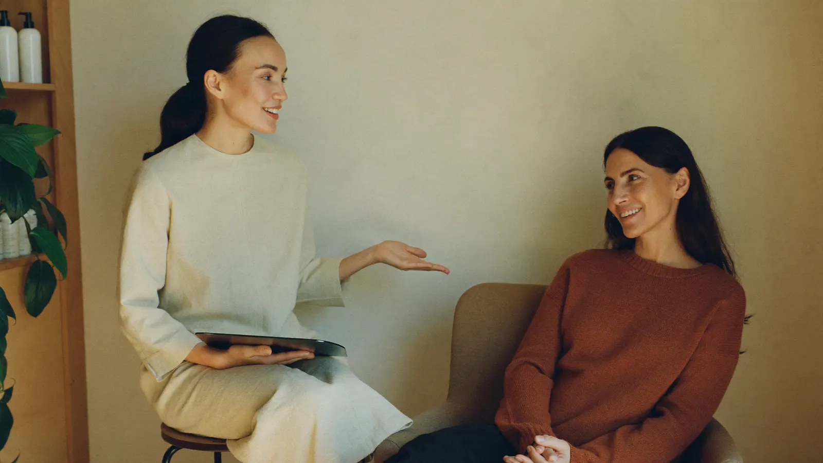 Aesthetician talking through a program plan on a tablet with a client in a med spa consultation room.